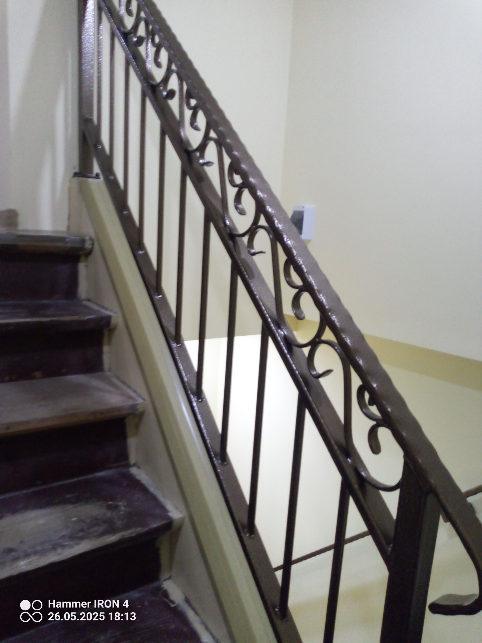 Kute, brązowe balustrady schodowe z dekoracyjnymi elementami, widoczne z dołu. Schody drewniane, ściany jasne. Detal wykonania.