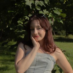 Kasia Krupa - Portret kobiety w dżinsowym gorsecie na tle zieleni, z okularami na włosach. Delikatne światło podkreśla rysy twarzy, a naturalne tło dodaje swobody.