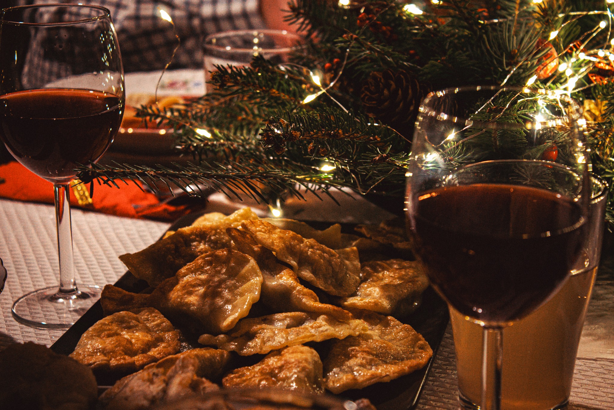 Świąteczny stół: pierogi na czarnym talerzu, dwa kieliszki czerwonego wina i stroik ze światełkami tworzą ciepłą, domową atmosferę.