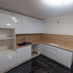 Meble kuchenne z pasją - Nowoczesna kuchnia z białymi szafkami i drewnianym blatem, czarny zlew i marmurowa podłoga. Minimalistyczny design, oświetlenie sufitowe.