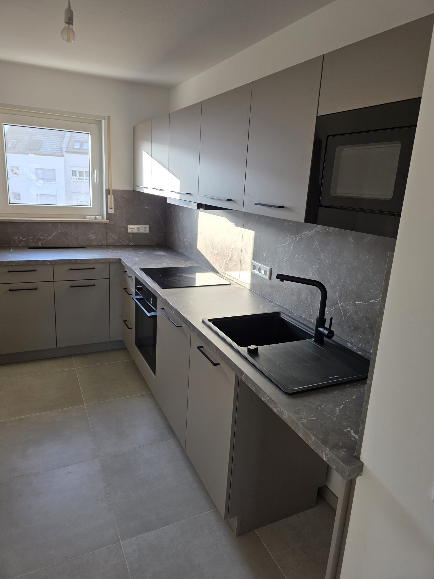Nowoczesna kuchnia w odcieniach szarości z blatem imitującym marmur, czarna armatura i oświetlenie. Realizacja w Jeleniej Górze. Minimalistyczny design.
