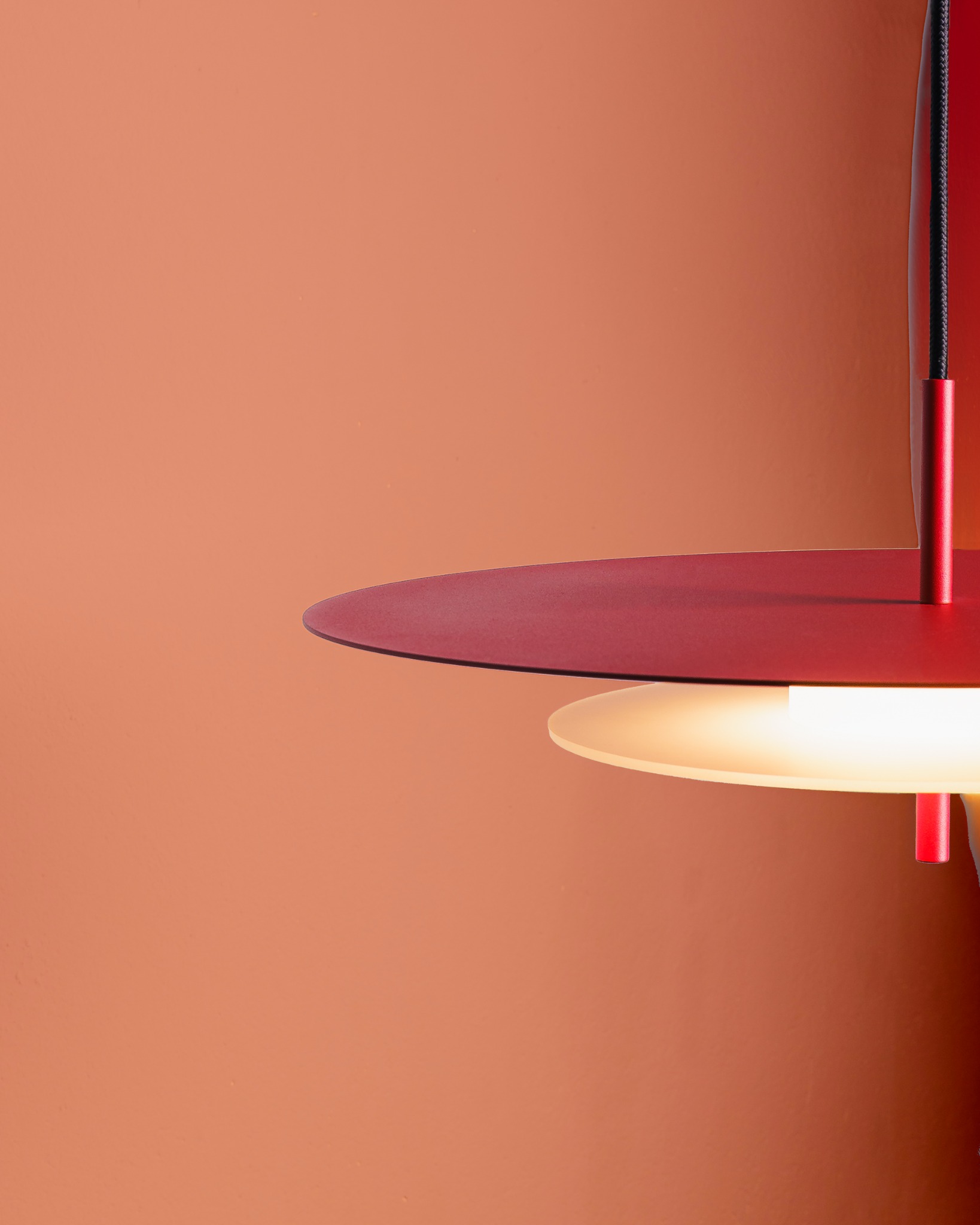 Nowoczesna lampa wisząca z czerwonymi, okrągłymi kloszami i ciepłym światłem na tle ściany w kolorze terakoty. Minimalistyczny design, oświetlenie wnętrz.