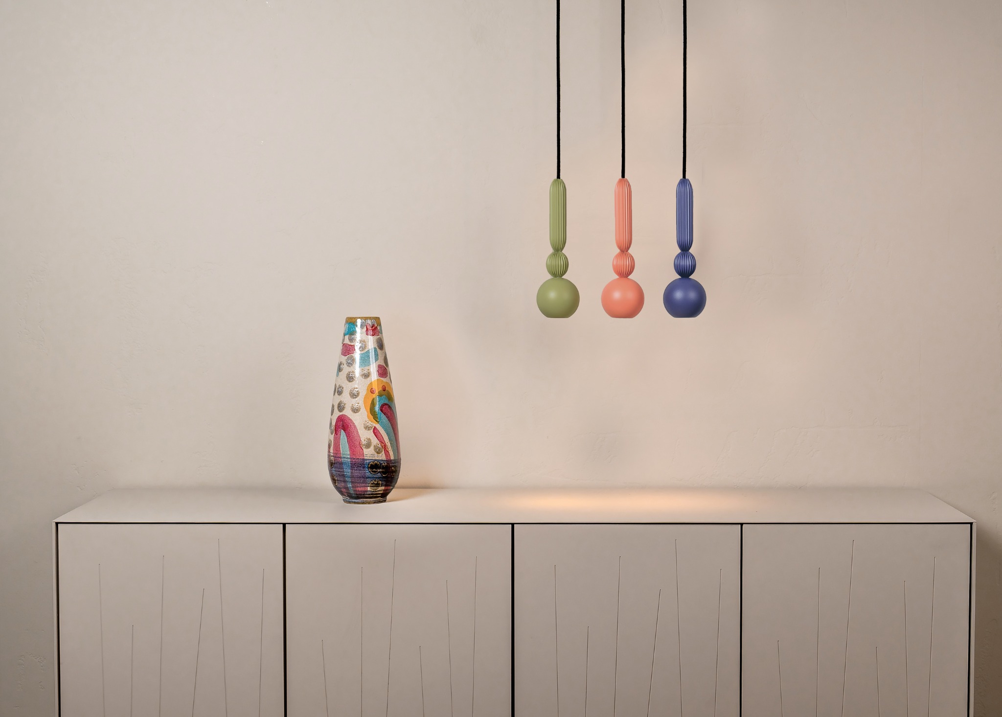 Kolorowe lampy wiszące w stylu retro i wzorzysty wazon na szafce, tworzące unikalną kompozycję wnętrza. Pastelowe barwy i nowoczesny design.