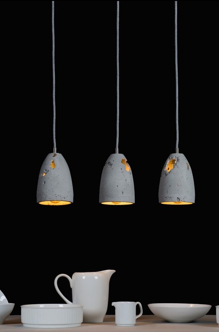 Trzy betonowe lampy wiszące z żółtym światłem na tle czerni, poniżej biała ceramika. Unikalny design z widocznymi niedoskonałościami betonu.