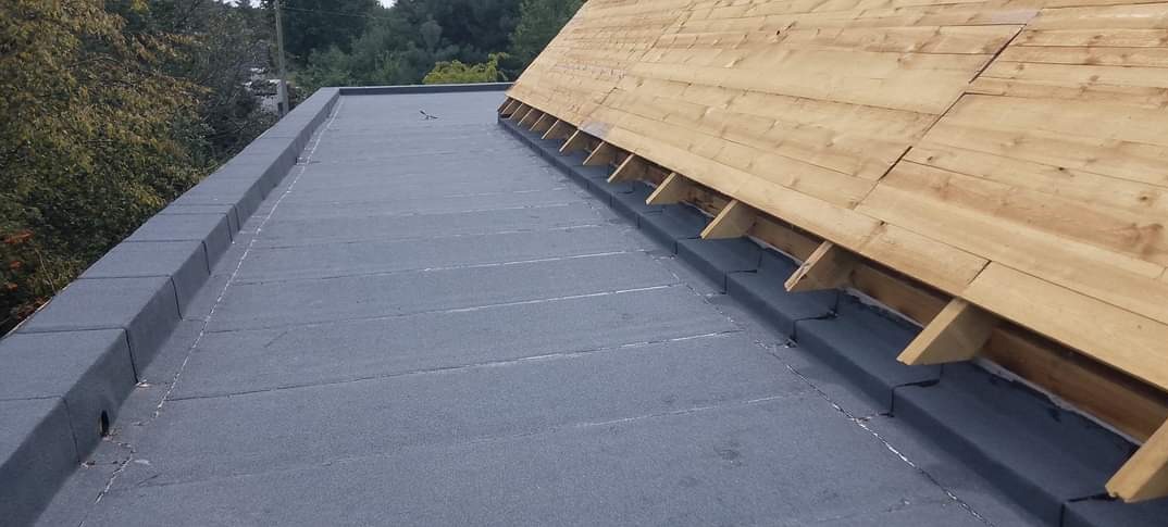 Szczegółowe ujęcie płaskiego dachu pokrytego papą, z widocznymi obróbkami blacharskimi i elementami konstrukcji drewnianej. Dach w trakcie prac wykończeniowych.
