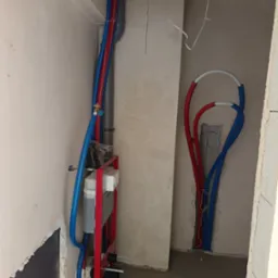 Montaż instalacji wodnej: czerwone i niebieskie rury prowadzone wzdłuż ściany, instalacja podtynkowa WC na metalowym stelażu, surowy stan.