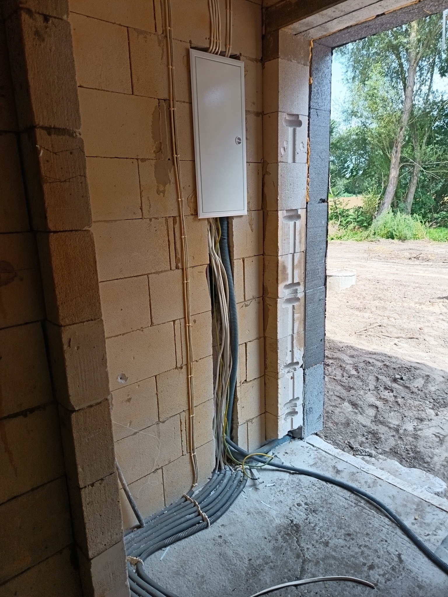 Rozdzielnia elektryczna natynkowa z przewodami w karbowanych peszlach, zamontowana na ścianie z bloczków betonu komórkowego w nowo budowanym budynku.