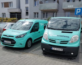 Dwa turkusowe busy z logo firmy 'Air Masters' zaparkowane przed budynkiem. Jeden to Ford Transit Connect, drugi to Nissan Primastar. Tablice rejestracyjne widoczne.