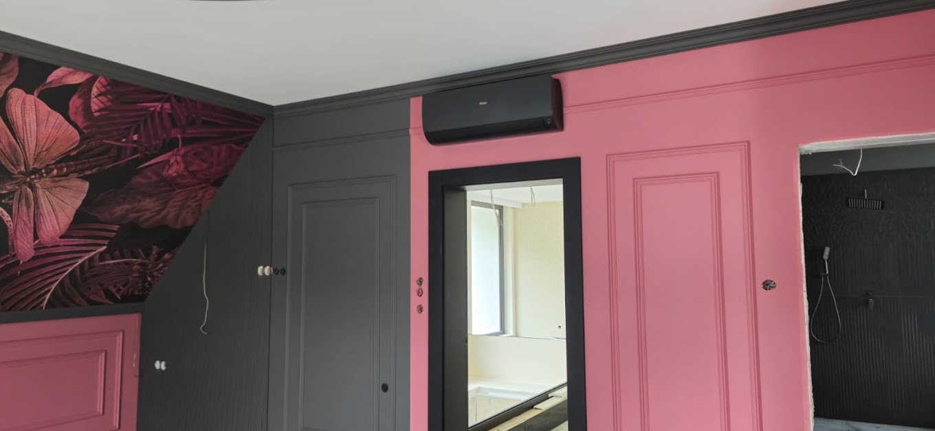 Czarna klimatyzacja na różowej ścianie z dekoracyjnymi panelami w nowocześnie urządzonym wnętrzu z szarymi elementami i wzorzystą tapetą.