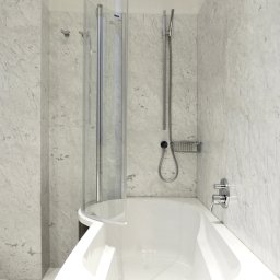 Łazienka z wanną z parawanem nawannowym firmy Dusholux. Architekt wnętrz Anna Buczny do aranżacji łazienki wykorzystała marmur bianco carrara i drewno wenge. Łazienka znajduje się w eklektycznej kamienicy w centrum Szczecina.