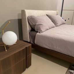 ANNA BUCZNY PIĘKNE WNĘTRZA - Nowoczesna sypialnia: łóżko z tapicerowanym wezgłowiem, drewniana szafka nocna z lampką w kształcie kuli. Minimalistyczny design, stonowana kolorystyka, dywan z geometrycznym wzorem.