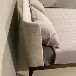 ANNA BUCZNY PIĘKNE WNĘTRZA - Beżowe łóżko z tapicerowanym wezgłowiem i lnianą pościelą w minimalistycznej sypialni. Widok z boku, z bliska na wezgłowie i pościel. Stonowana kolorystyka.