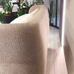 ANNA BUCZNY PIĘKNE WNĘTRZA - Beżowa sofa z poduszką w minimalistycznym wnętrzu z roślinami. Widok z boku, ukazujący fakturę tapicerki i subtelne oświetlenie.