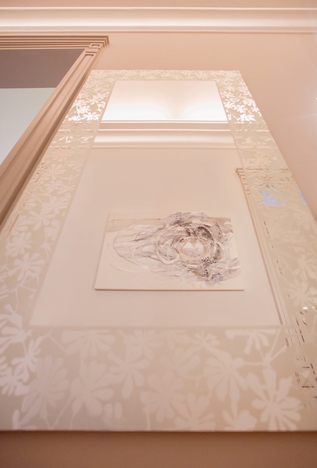 Nowoczesna aranżacja wnętrza: abstrakcyjny obraz na ścianie w dekoracyjnej, podświetlanej ramie z motywem kwiatowym. Całość utrzymana w jasnej, kremowej kolorystyce.