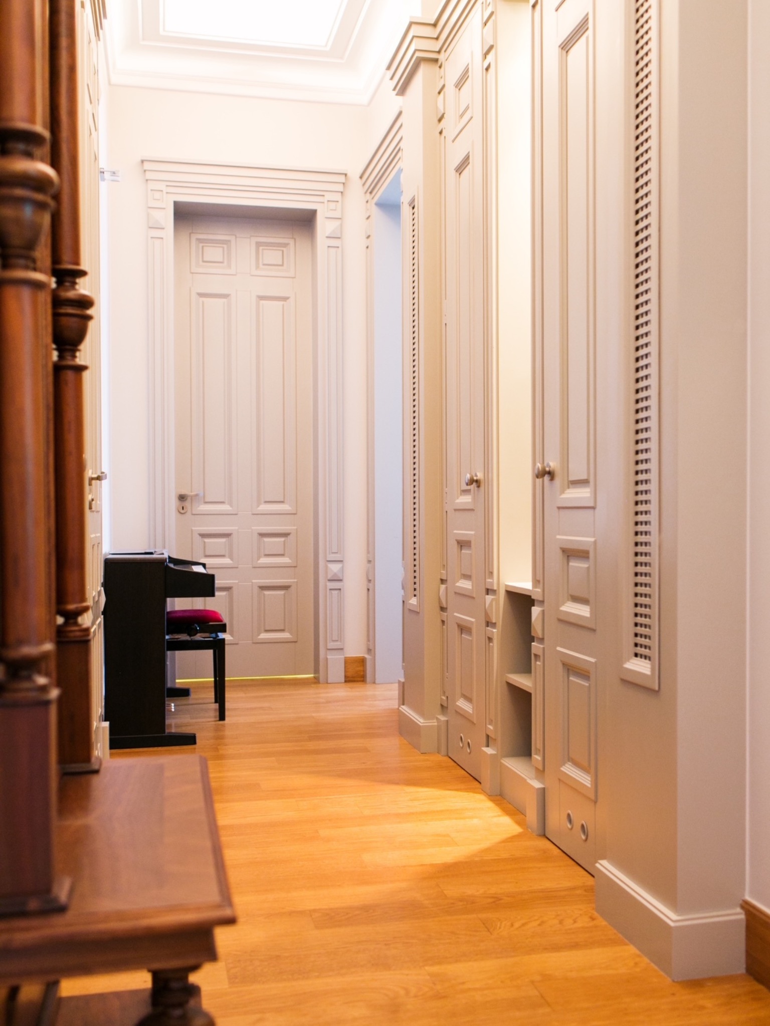 Korytarz w mieszkaniu po liftingu w stylu vintage: drewniana podłoga, zabudowa szaf z ażurowymi detalami, drzwi z płycinami, pianino. Projekt wnętrz.