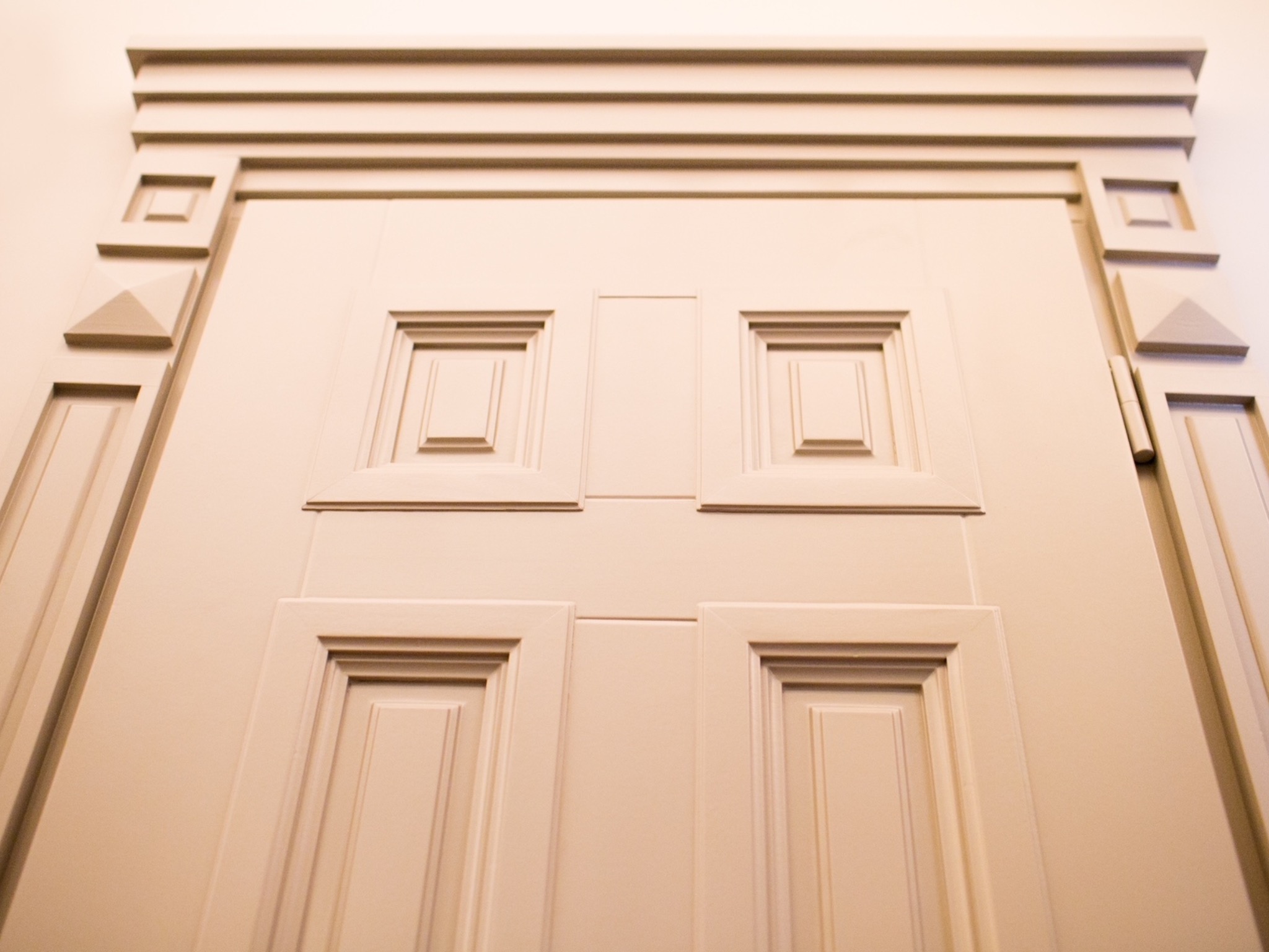 Beżowe, klasyczne drzwi wewnętrzne z dekoracyjnymi płycinami i geometrycznymi zdobieniami, widziane z dołu, podkreślające ich wysokość i detal.