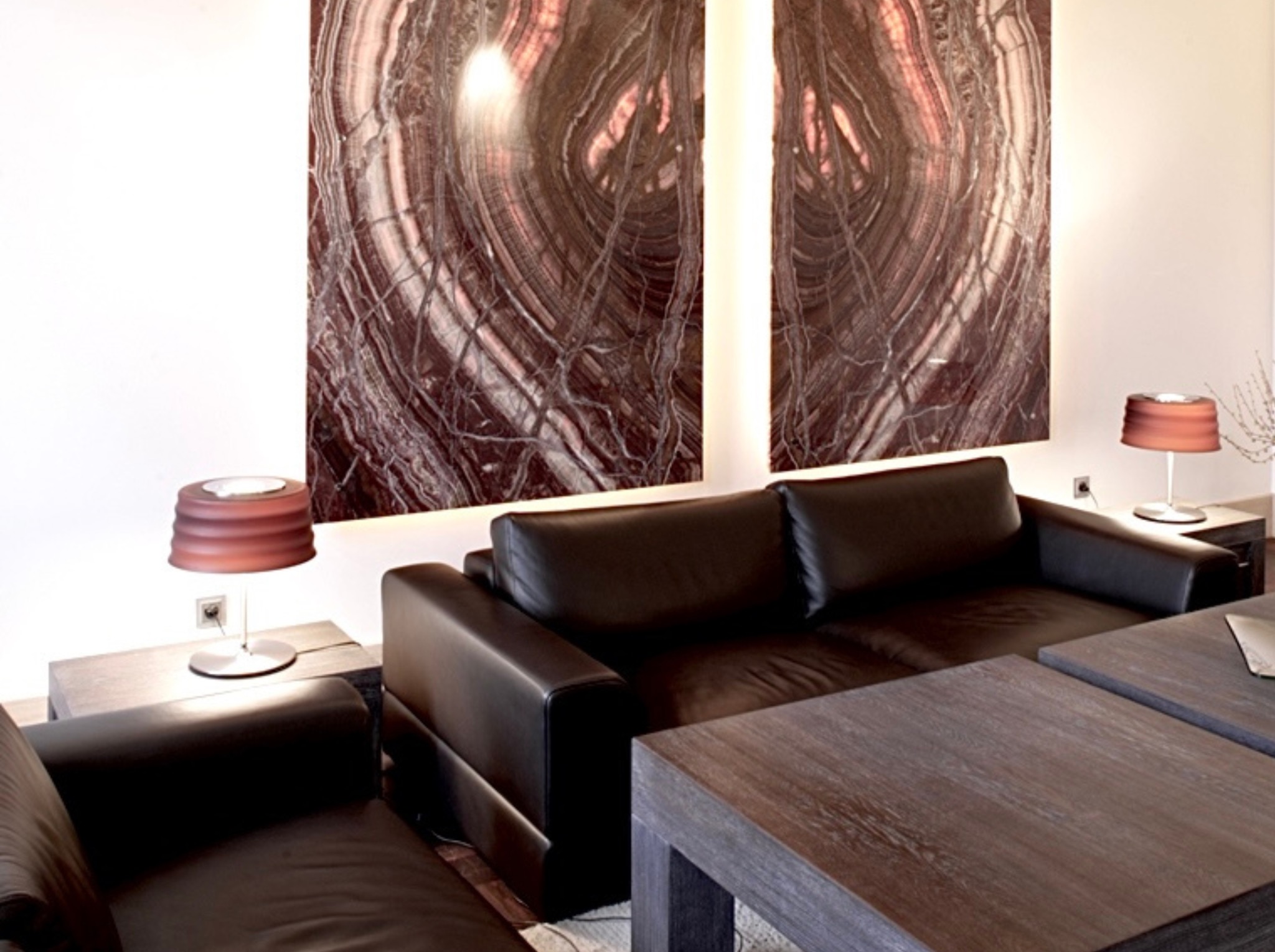 Salon z czekoladową skórzaną sofą i stolikami z ciemnego drewna. Na ścianie dwie podświetlane płyty onyksu z unikalnym wzorem. Lampki stołowe z abażurami.