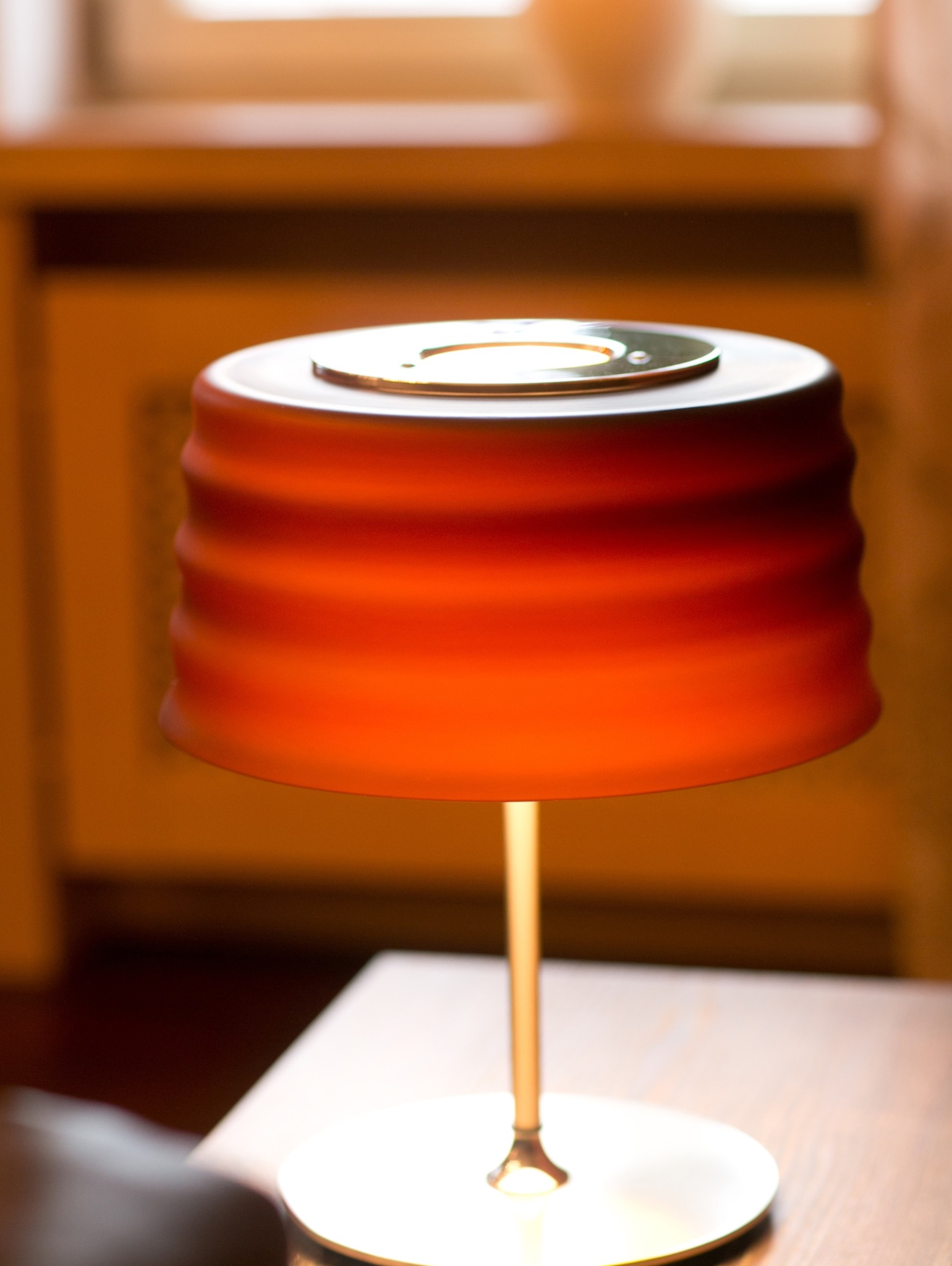 Lampa stołowa z pomarańczowym abażurem w salonie. Ciepłe światło podkreśla aranżację wnętrza. Widoczne detale i delikatne oświetlenie.