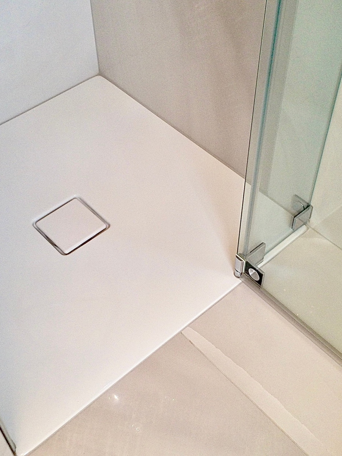 Biały brodzik z odpływem liniowym i szklaną kabiną prysznicową, minimalistyczny design, jasne płytki podłogowe, chromowane okucia, nowoczesna łazienka.