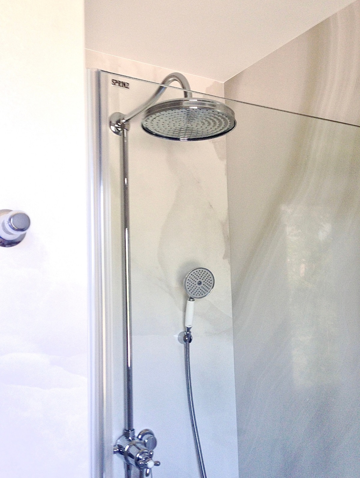 Nowoczesna kabina prysznicowa z deszczownicą i słuchawką, chromowana armatura, jasne płytki imitujące marmur. Minimalistyczny design.