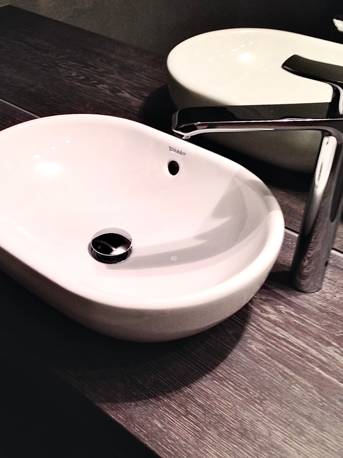 Biała, owalna umywalka nablatowa Duravit z chromowaną baterią na blacie z olejowanego forniru o wyraźnym rysunku drewna. Minimalistyczny design, nowoczesna łazienka.