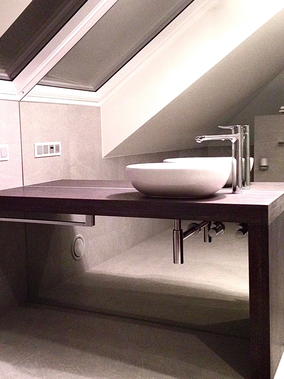 Nowoczesna łazienka ze skosami: blat z forniru, umywalka nablatowa, chromowana bateria. Minimalistyczny design, stonowana kolorystyka, oświetlenie punktowe.