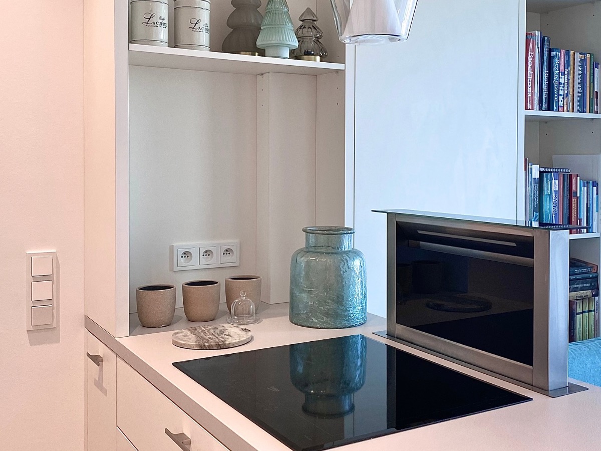 Nowoczesna kuchnia z płytą indukcyjną, szklanym wazonem i dekoracjami świątecznymi na półce. Minimalistyczny design, jasne kolory i subtelne oświetlenie.