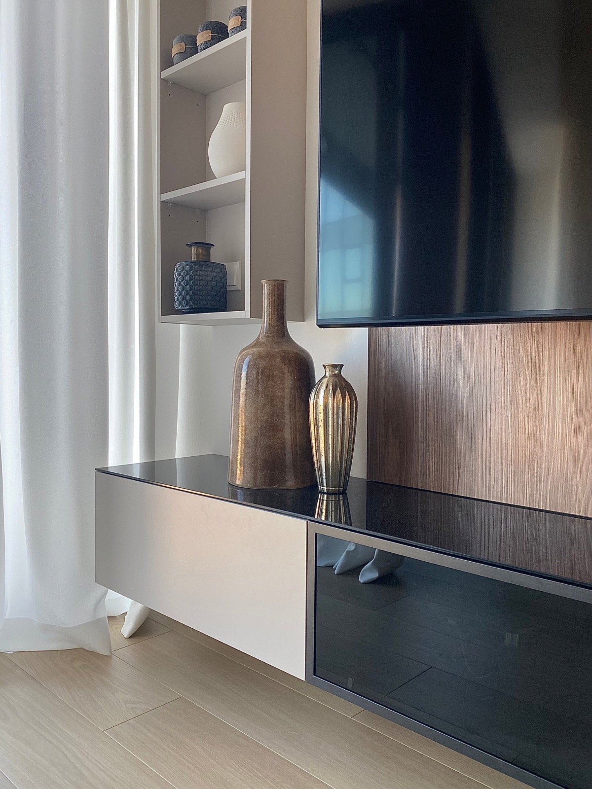 Nowoczesna aranżacja salonu w Szczecinie: szafka RTV z czarnym blatem, dekoracyjne wazony, telewizor i subtelna zasłona. Minimalistyczny design.