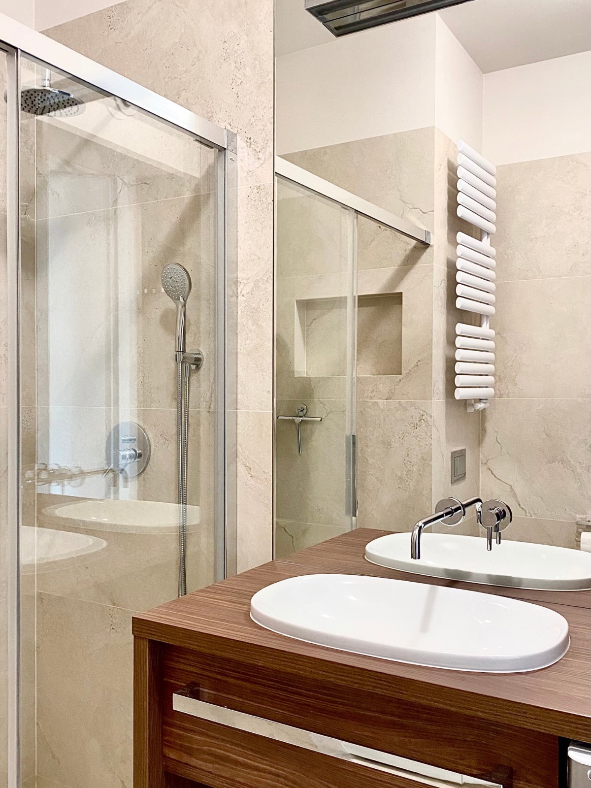 Nowoczesna łazienka w Szczecinie z kabiną prysznicową, umywalką na drewnianym blacie i grzejnikiem drabinkowym. Beżowe płytki imitujące kamień.