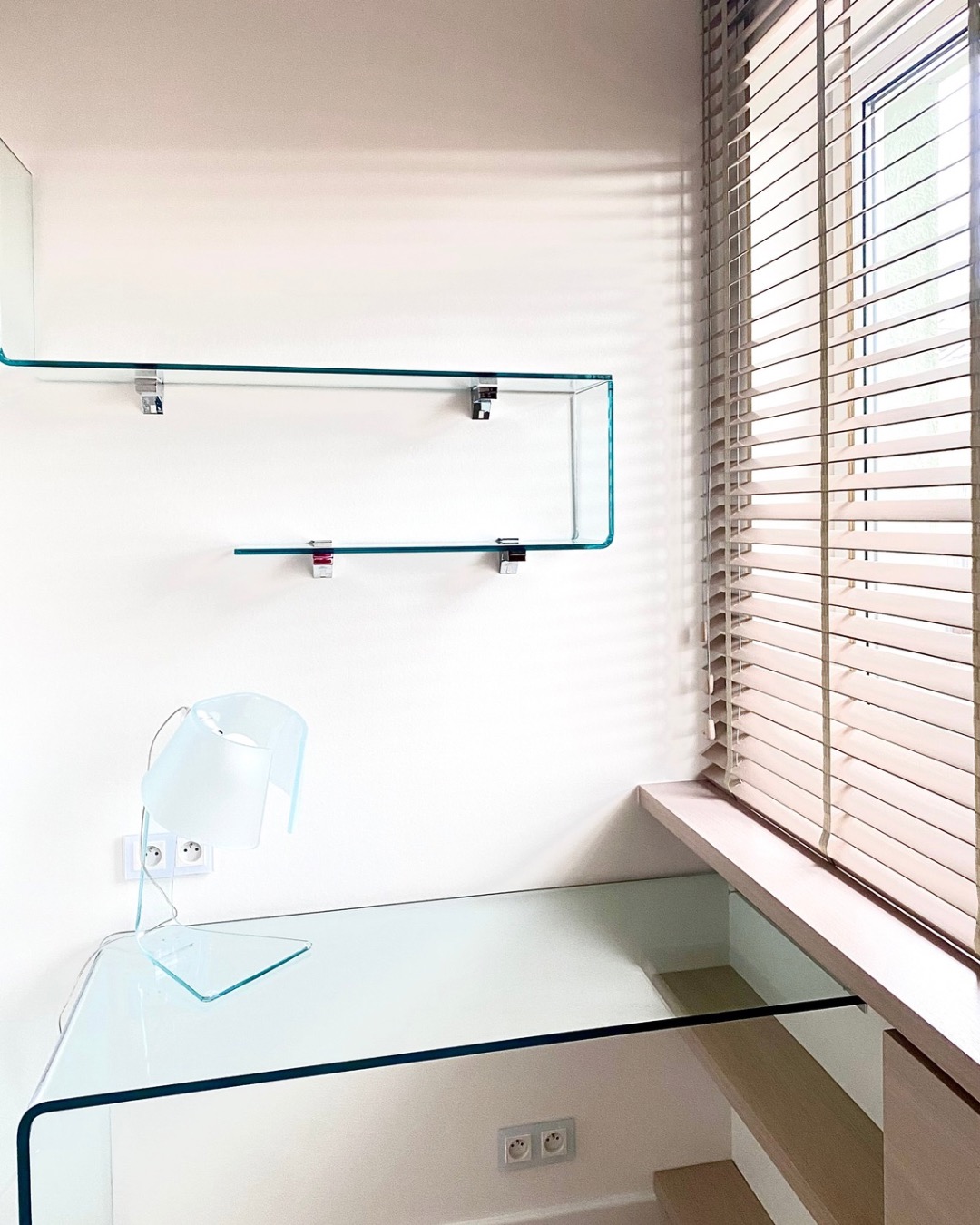 Szklane biurko i półki Fiam Italia w domowym biurze. Minimalistyczny design z lampką biurkową. Żaluzje drewniane w oknie. Realizacja architekta wnętrz.