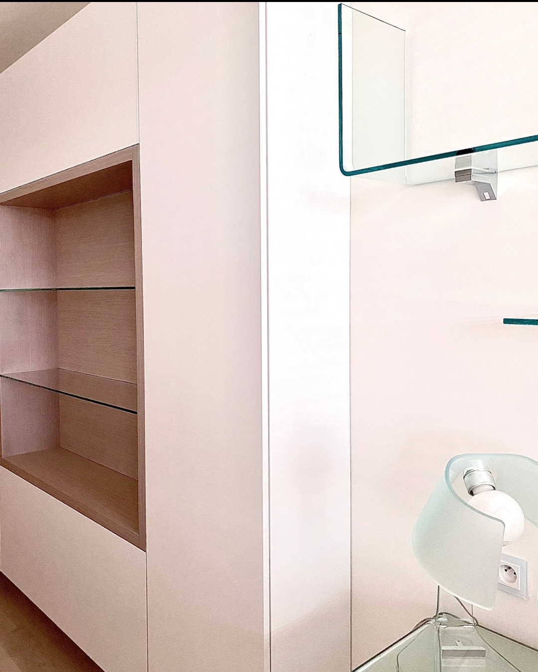 Nowoczesny gabinet: zabudowa meblowa z półkami z przezroczystego szkła, minimalistyczna lampa na szklanym stoliku, jasne ściany. Detal aranżacji wnętrza.