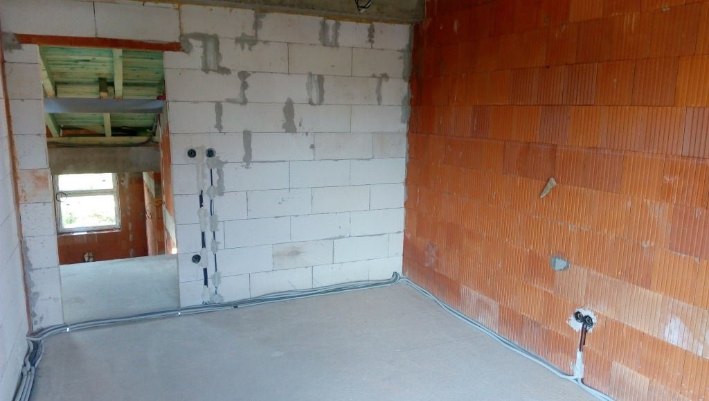 Wnętrze w trakcie prac elektrycznych: kable w peszlach ułożone wzdłuż ścian, puszki elektryczne zamontowane w ścianie z betonu komórkowego i cegły ceramicznej.