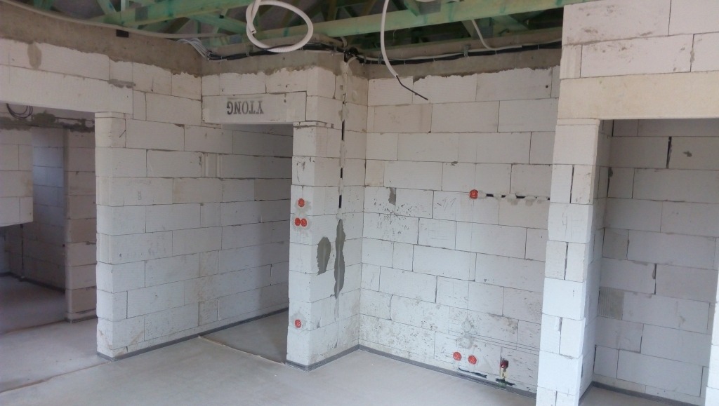 Wnętrze w trakcie budowy z białymi ścianami z betonu komórkowego. Widoczne przewody elektryczne w ścianach i pod sufitem. Surowy stan, brak wykończenia.