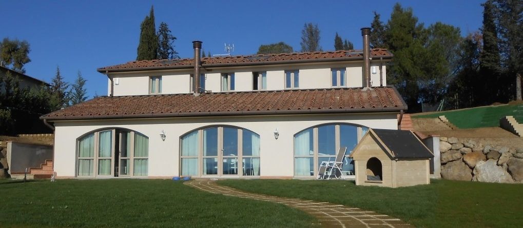 Dwukondygnacyjny dom z beżową elewacją i brązowym dachem, widoczny z ogrodu z trawnikiem i ścieżką. Na pierwszym planie buda dla psa.