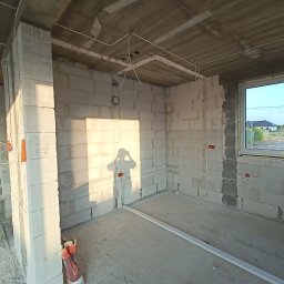 Piotr Gańko - Wnętrze w stanie surowym z widoczną instalacją elektryczną: kable poprowadzone po ścianach z betonu komórkowego i suficie. Widoczne puszki elektryczne i cień osoby.