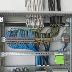 Rozdzielnica elektryczna z precyzyjnie ułożonymi przewodami, oznaczonymi etykietami. Widoczne złącza i elementy montażowe. Na zielonej kartce notatka: RB 1.2, AS-212.