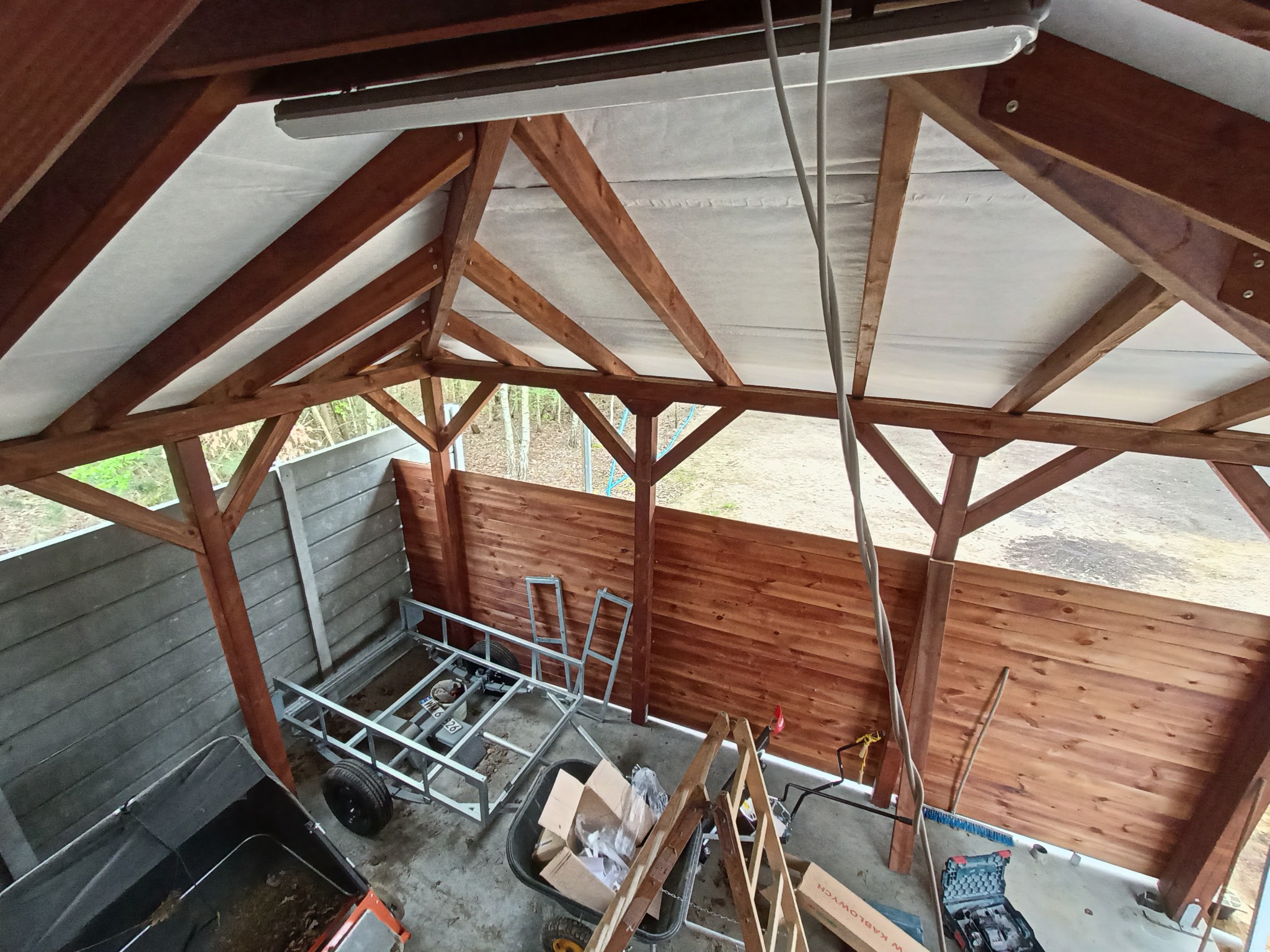 Wnętrze drewnianej konstrukcji z oświetleniem, w trakcie budowy lub remontu. Widoczne narzędzia i materiały budowlane, drewniane elementy konstrukcyjne.