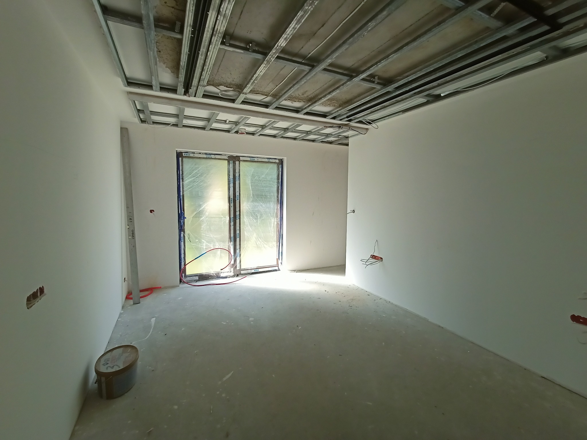 Wnętrze w trakcie prac wykończeniowych w Mińsku Mazowieckim: widoczne profile sufitowe, instalacja elektryczna w ścianach, okno zabezpieczone folią.