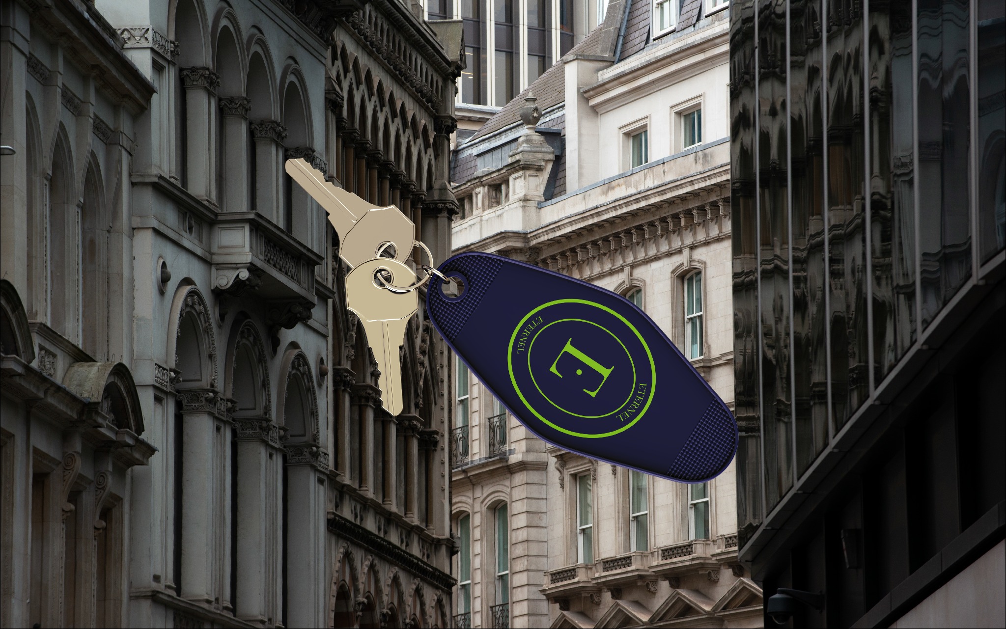 Klucze z brelokiem na tle fasady kamienicy z balkonami i kolumnami, w tle nowoczesny budynek biurowy z odbiciem. Brelok z logo.