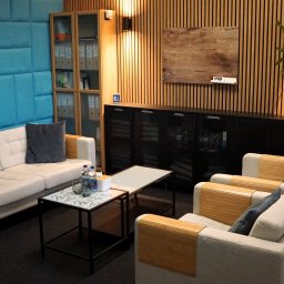 PsycheClinic - Profesjonalna Psychoterapia i Wsparcie Psychologiczne Psycholog Warszawa Bemowo - Klimatyczne wnętrze gabinetu z sofą, fotelami i stolikami kawowymi. W tle drewniane panele ścienne i szafki z dokumentami. Dyskretne oświetlenie tworzy przytulną atmosferę.