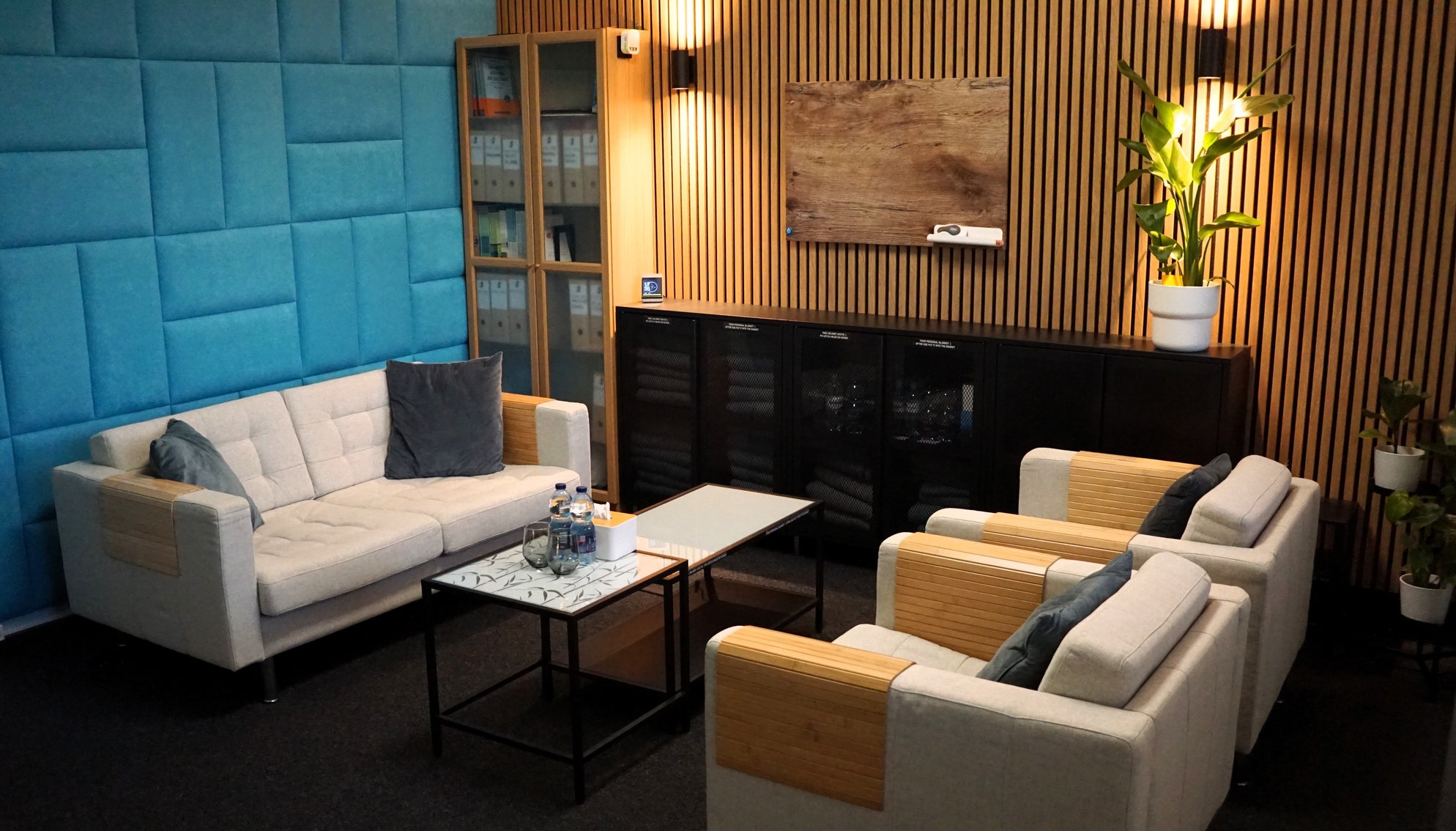 Klimatyczne wnętrze gabinetu z sofą, fotelami i stolikami kawowymi. W tle drewniane panele ścienne i szafki z dokumentami. Dyskretne oświetlenie tworzy przytulną atmosferę.