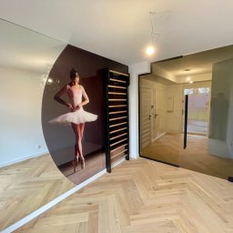 KM Glass - Nowoczesne wnętrze z lustrem z motywem baletnicy i szklanymi drzwiami z czarną ramą, parkiet w jodełkę. Widoczny fragment osoby robiącej zdjęcie.