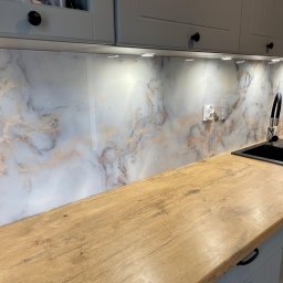 KM Glass - Szklany panel kuchenny z marmurkowym wzorem, oświetlony punktowo, zamontowany nad drewnianym blatem z czarnym zlewem i baterią. Nowoczesna aranżacja kuchni.