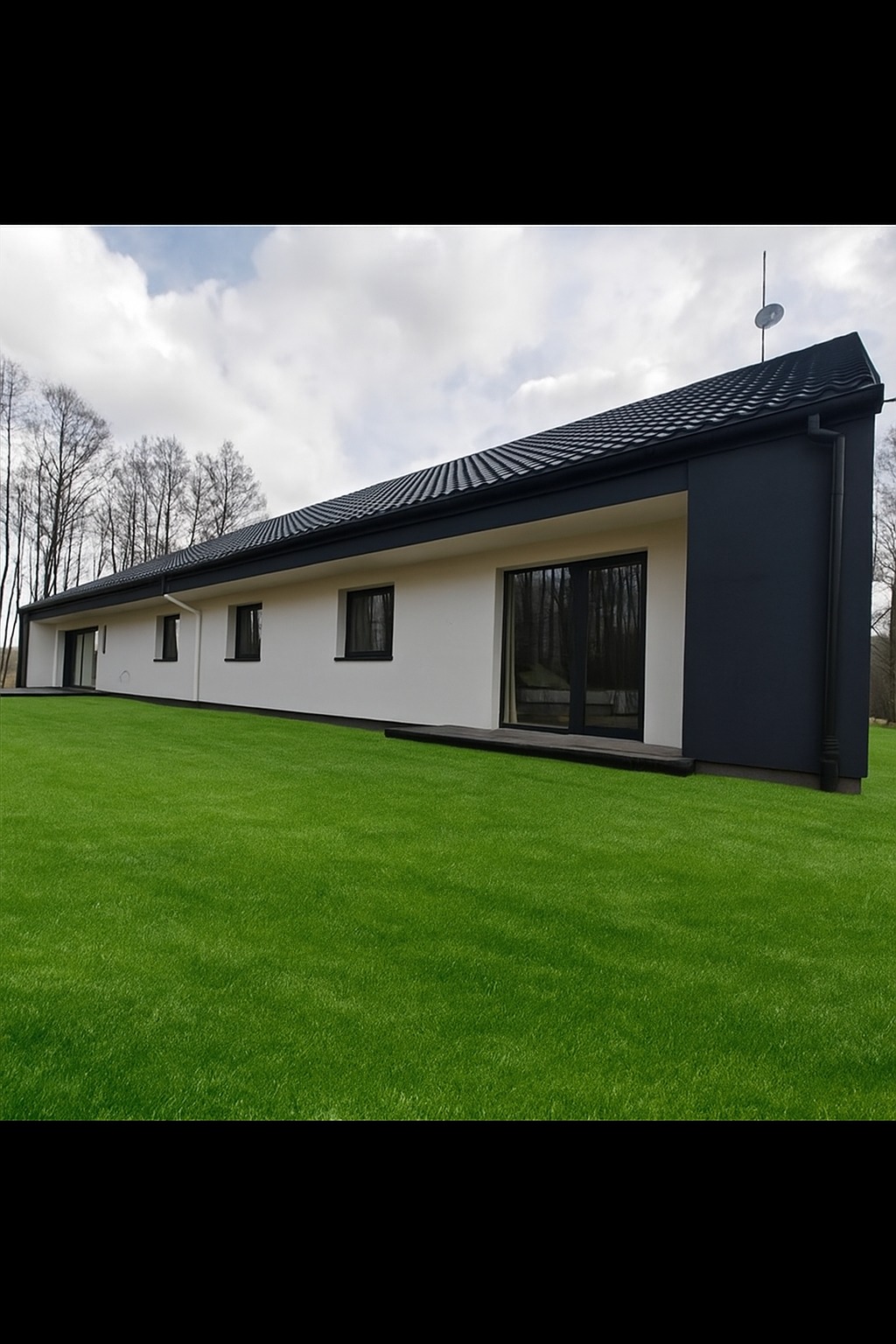 Nowoczesny, parterowy dom z białymi ścianami i ciemnymi akcentami architektonicznymi na tle zielonego trawnika i błękitnego nieba z chmurami.