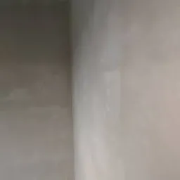 Wnętrze po tynkowaniu: gładkie, jasne ściany z widocznymi śladami świeżego tynku, sufit z odsłoniętą konstrukcją i fragment podłogi przy ścianie.