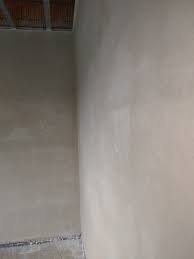 Wnętrze po tynkowaniu: gładkie, jasne ściany z widocznymi śladami świeżego tynku, sufit z odsłoniętą konstrukcją i fragment podłogi przy ścianie.