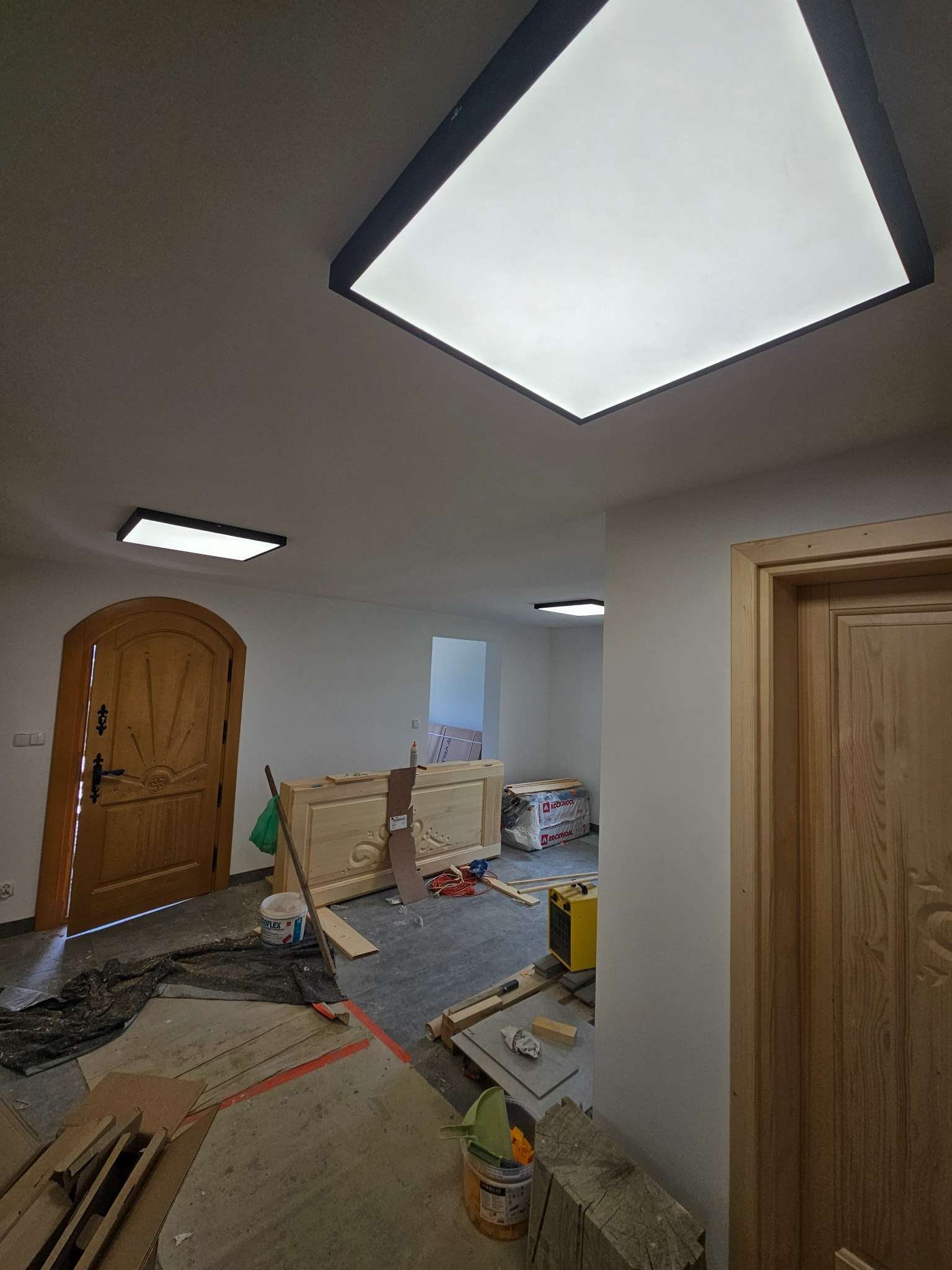 Nowoczesne, kwadratowe lampy sufitowe LED z czarną obwódką w jasnym wnętrzu w trakcie remontu. Widoczne narzędzia i materiały budowlane.