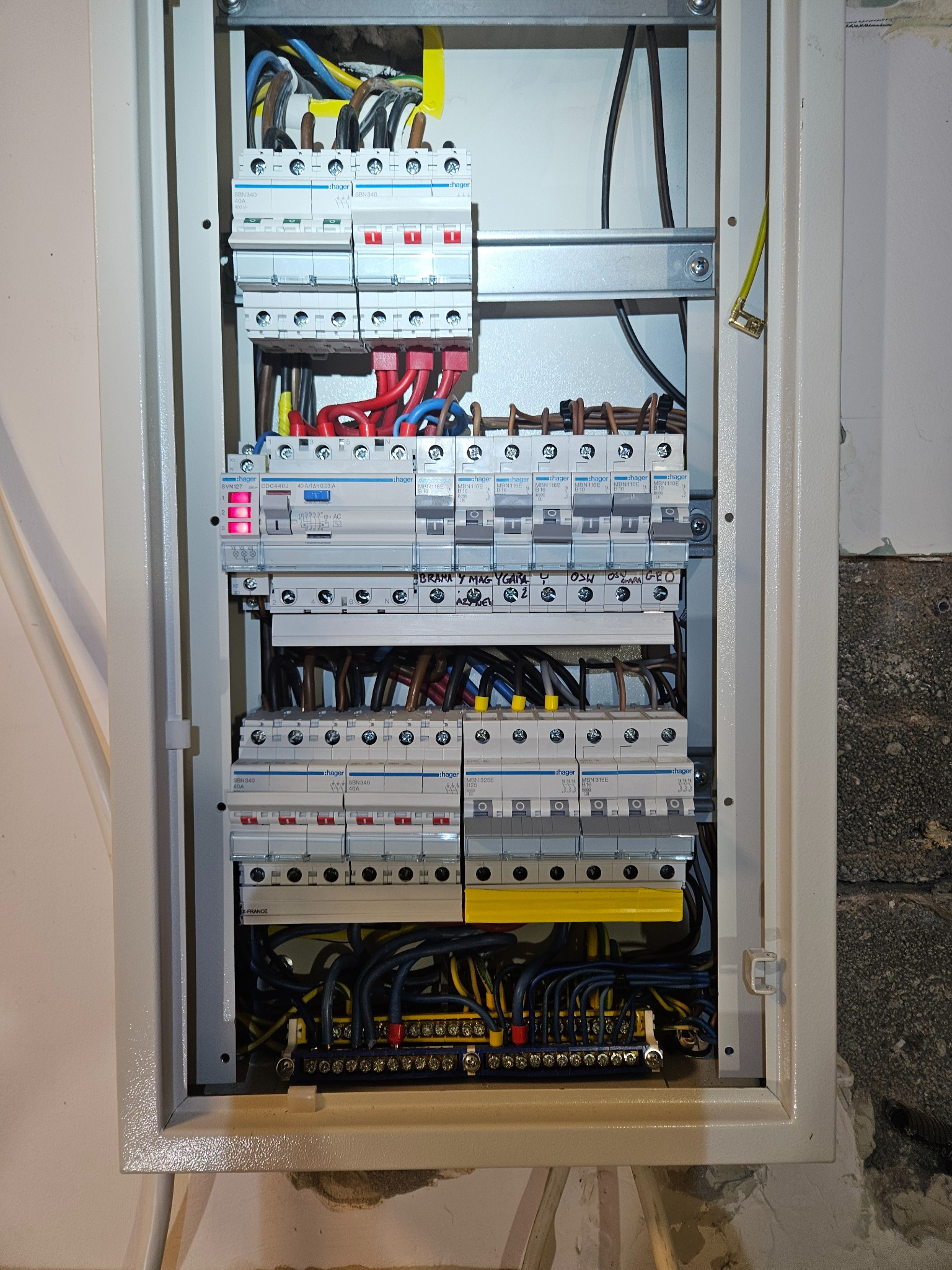 Rozdzielnica elektryczna z zainstalowanymi bezpiecznikami Hager, widoczne przewody i listwy zaciskowe. Napisy na obudowie.