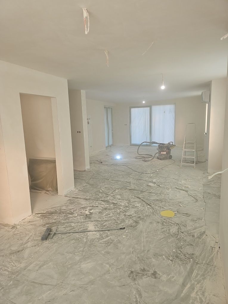 Wnętrze w trakcie prac wykończeniowych: świeżo pomalowane ściany, zakryta podłoga, widoczny sprzęt budowlany i drabina. Perspektywa z niskiego kąta.