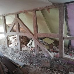 Adam Buszman Usługi Remontowo-Budowlane - Demontaż ściany działowej z cegły. Widoczne drewniane wzmocnienia i gruz. Etap prac remontowych z usuniętymi elementami konstrukcyjnymi i pozostałościami po ścianie.